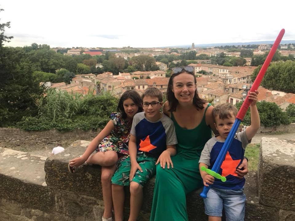 Eve and her three children are smiling and sitting on a wall overlooking Avignon. 