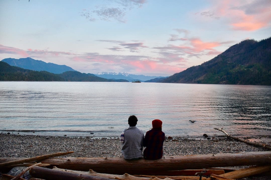 Picture shows a couple with their backs to the camera overlooking a lake